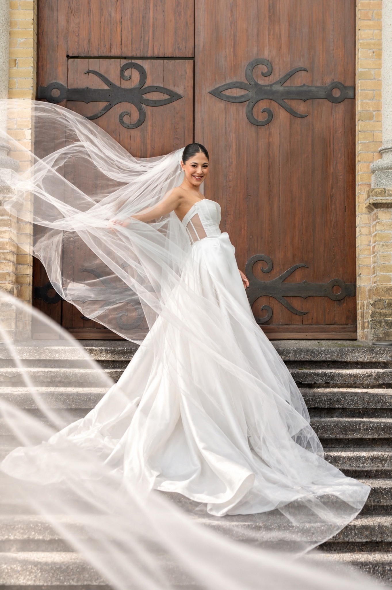 Novia con velo en movimiento frente a puertas de madera; fotografía de Jossie García